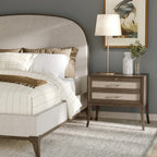 Neatly made bed with a nightstand featuring a lamp and decorative items in a bedroom setting.