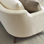 Close-up of a beige armchair with a textured surface and wooden legs on a neutral background.