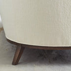 Close-up of a beige upholstered chair with wooden legs on a carpeted floor.