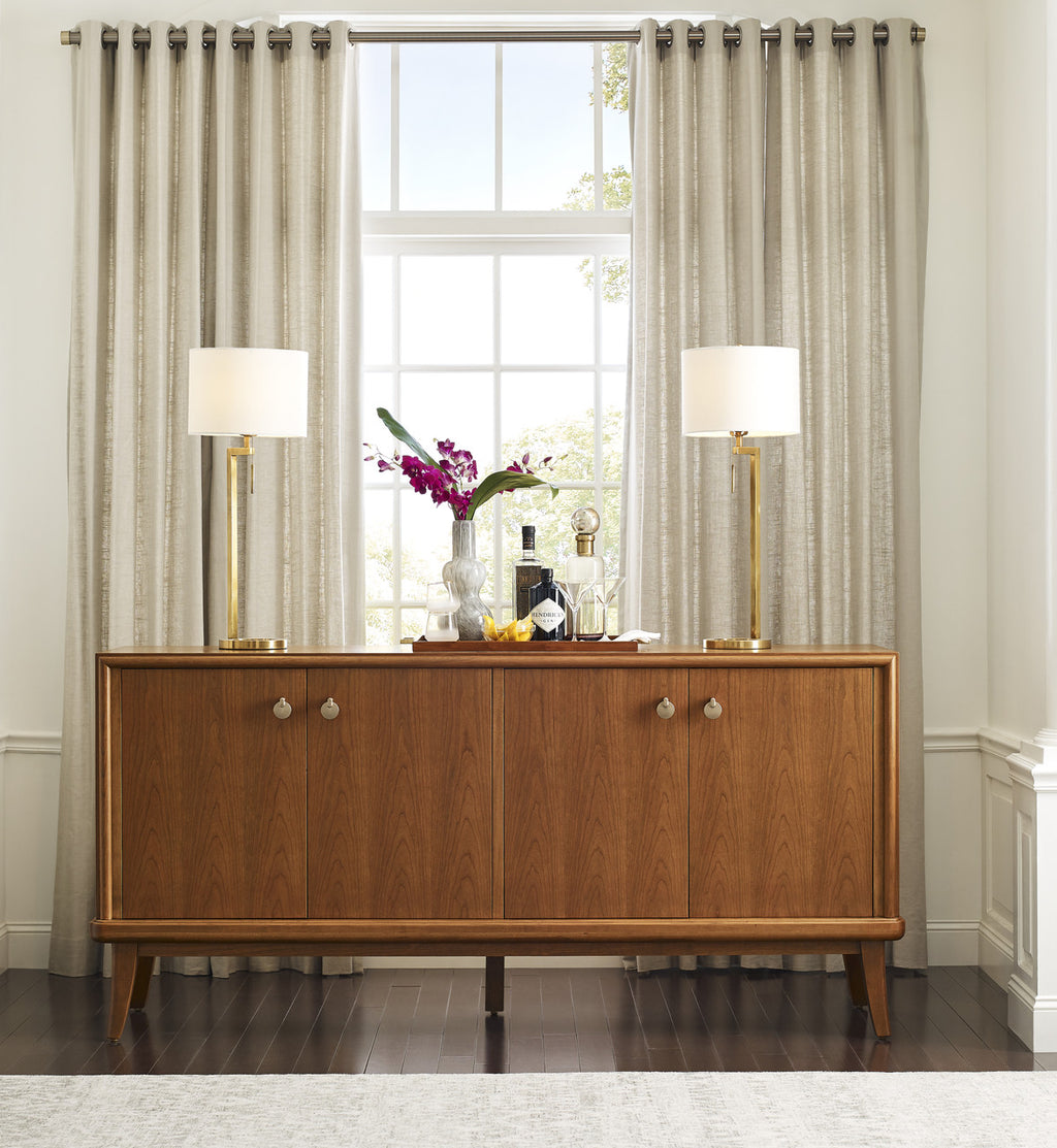 Wooden sideboard with lamps and decorative items against a window with curtains.