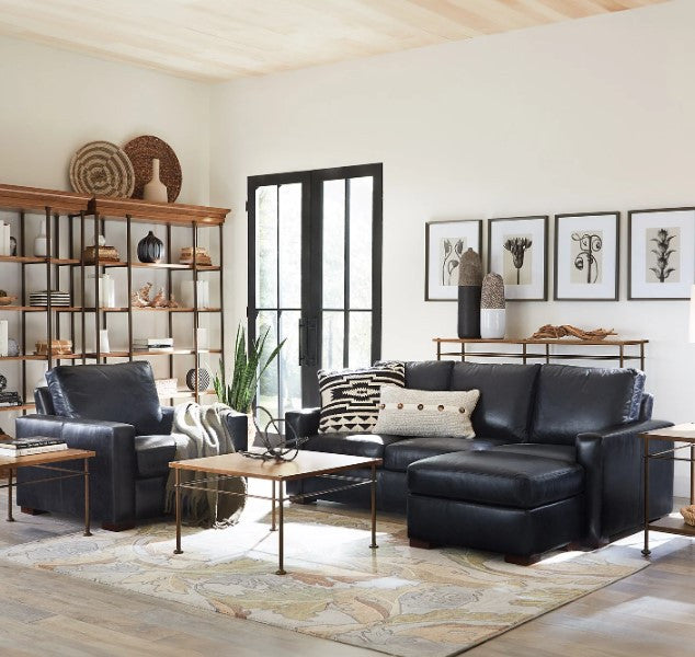 Modern living room with black leather sectional sofa, coffee table, and decorative items.