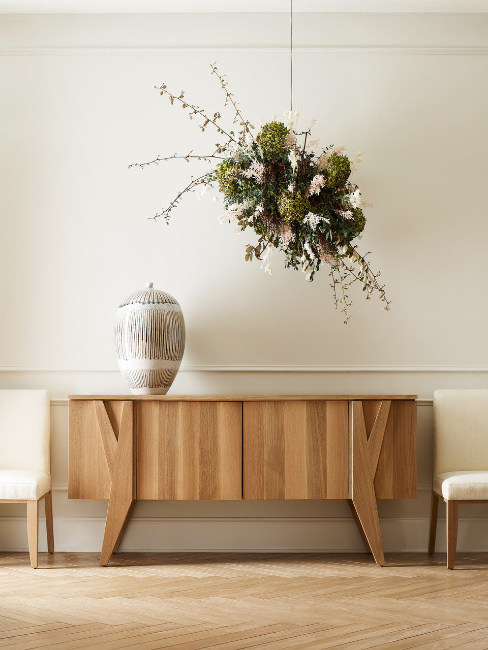 Wooden sideboard with decorative vase and floral arrangement against a white wall.