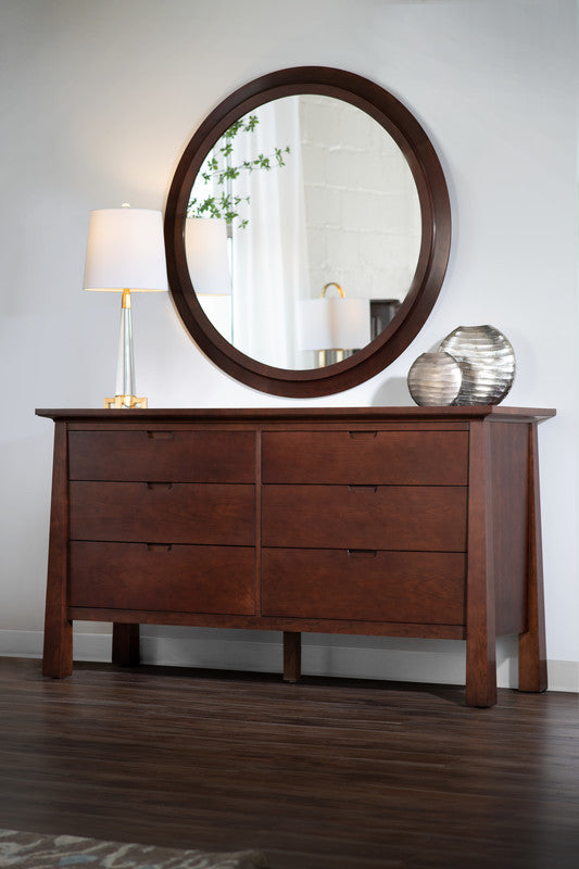 Wooden dresser with round park slope mirror and decorative items in a room setting