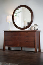 Wooden dresser with round park slope mirror and decorative items in a room setting