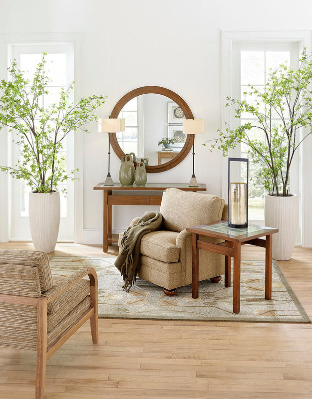 Living room with beige sofa, wooden coffee table, and decorative plants. The park slope mirror looms over the table. 
