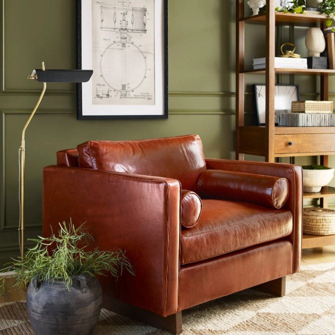 Brown leather sofa in a room with green walls, a floor lamp, and a bookshelf.