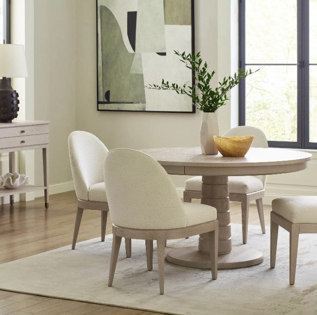 Dining room with a round wooden table and white cushioned chairs.