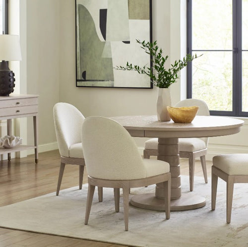 Dining room with a round wooden table and white cushioned chairs.