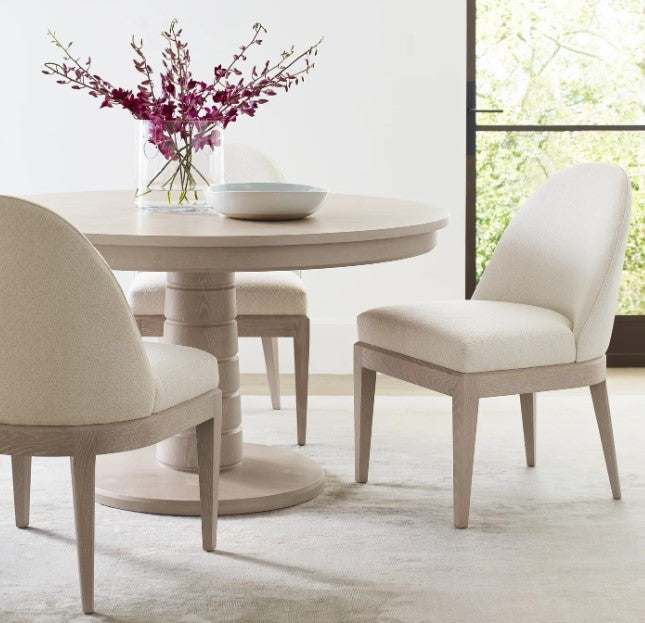 Round dining table with chairs and a vase of flowers in a bright room.