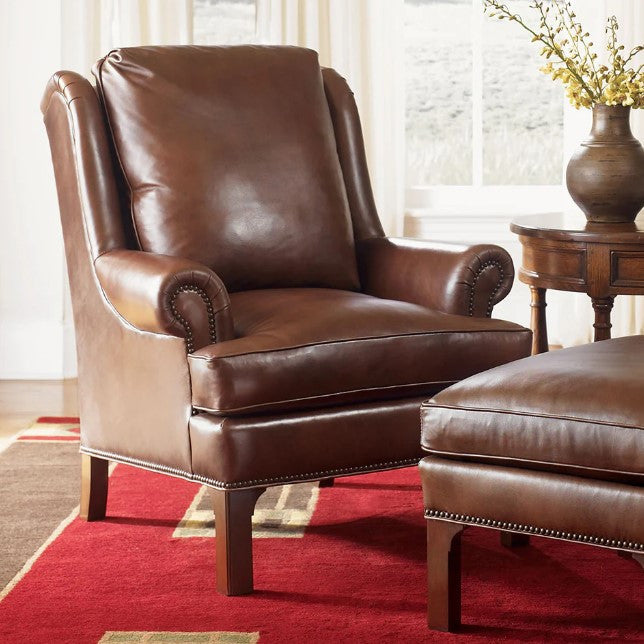 Brown leather armchair and ottoman on a red rug with a side table and plant in the background.
