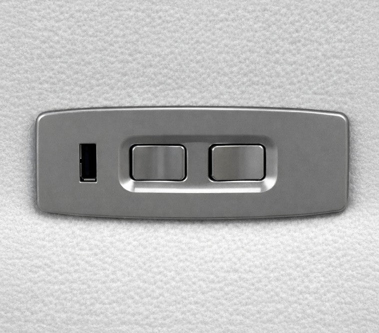 A rectangular brushed metal control panel with two toggle switches and a small vertical port, shown against a textured white background.