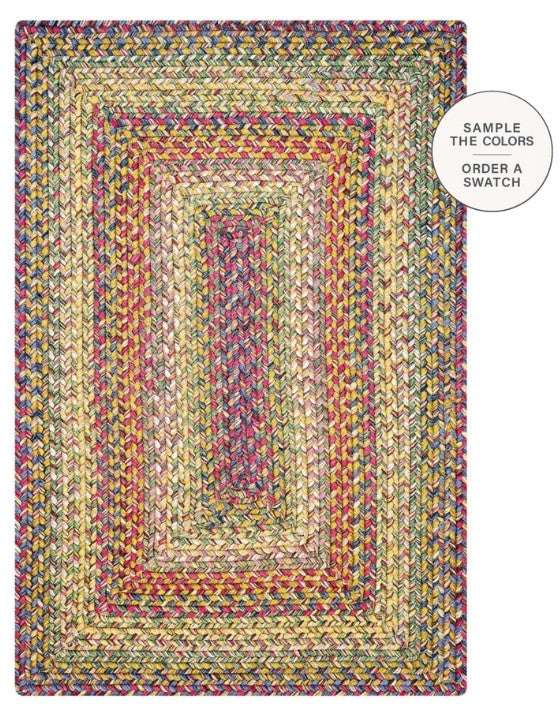 A rectangular braided area rug with concentric rectangular patterns, featuring a multicolor mix of yellow, green, blue, pink, and red yarns. A white circular badge in the top right corner reads 'SAMPLE THE COLORS ORDER A SWATCH'.