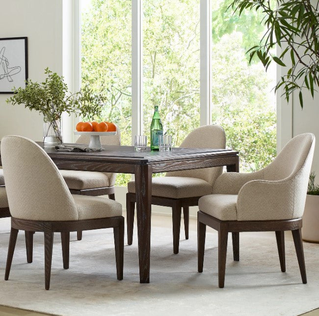Dining room with wooden table and chairs near large windows with a view of greenery.