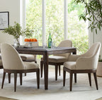 Dining room with wooden table and chairs near large windows with a view of greenery.