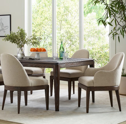 Dining room with wooden table and chairs near large windows with a view of greenery.