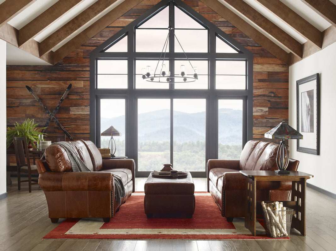 Cozy living room with brown leather furniture and large windows overlooking a scenic view.
