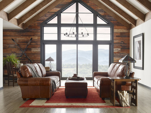 Cozy living room with brown leather furniture and large windows overlooking a scenic view.