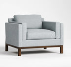 A light gray upholstered armchair with a dark wood base, shown from a three-quarter angle on a clean white studio background.