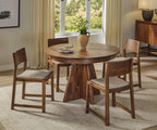A round wooden dining table with a carved pedestal base, surrounded by four matching wooden chairs with light beige upholstered seats, set in a bright dining room.