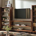 A dark brown wooden media console and shelving unit set, styled with books, vases, and a television mounted on the back wall in a warm, sunlit room.