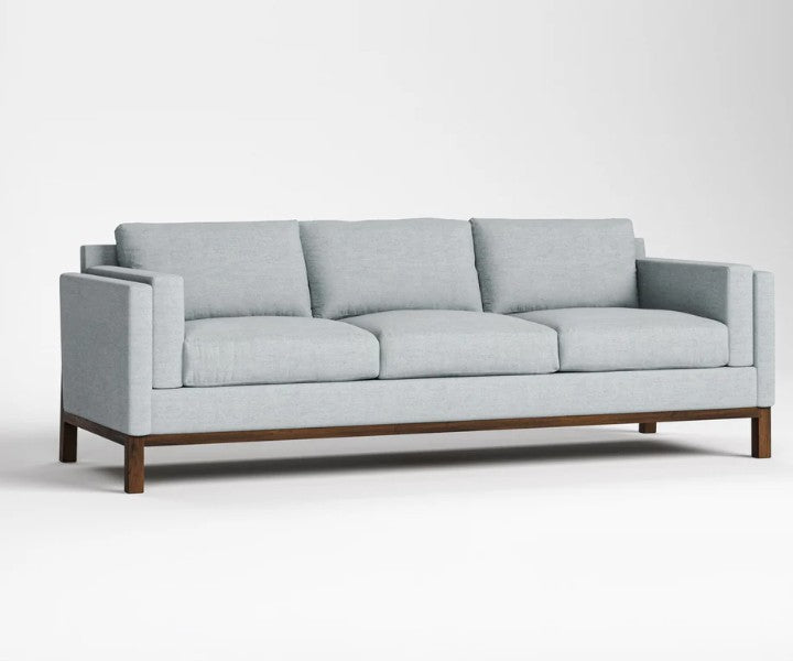 A three-seat sofa with light gray fabric upholstery and a dark brown wooden base, shown against a plain light gray studio background.