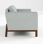 A modern light gray upholstered armchair with a dark brown wooden frame, shown from a side angle against a plain white studio background.