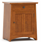 A mid-century modern wooden cabinet with a warm medium-brown finish, featuring a single drawer with a decorative metal knob and a single door with a matching knob, set against a plain white background.