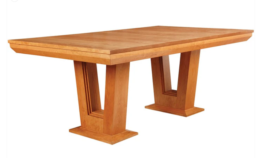 A rectangular wooden dining table with a warm medium-brown finish, featuring thick block-style pedestal legs with recessed panel details, shown on a plain white background.