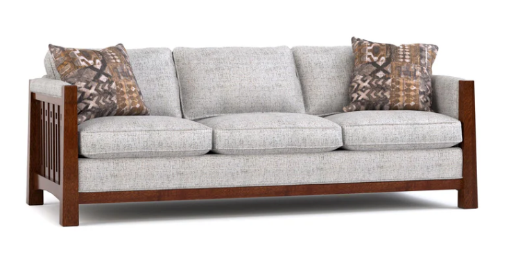 A three-seater sofa with light gray textured upholstery and a dark brown wooden frame, accented with two patterned throw pillows in brown, beige, and black.