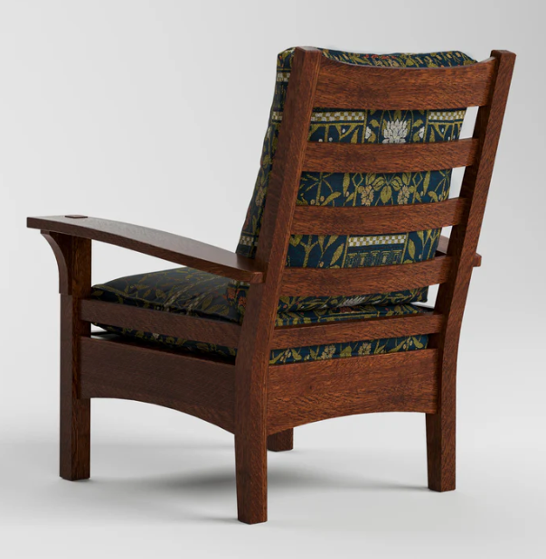 A wooden armchair shown from the back, featuring a dark brown wood frame and thick cushions with a navy blue and green botanical pattern.