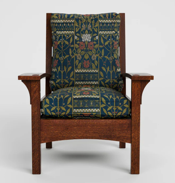 A classic Arts and Crafts style armchair with a dark reddish-brown wooden frame and thick, patterned fabric cushions featuring a botanical design in navy blue, green, and red.