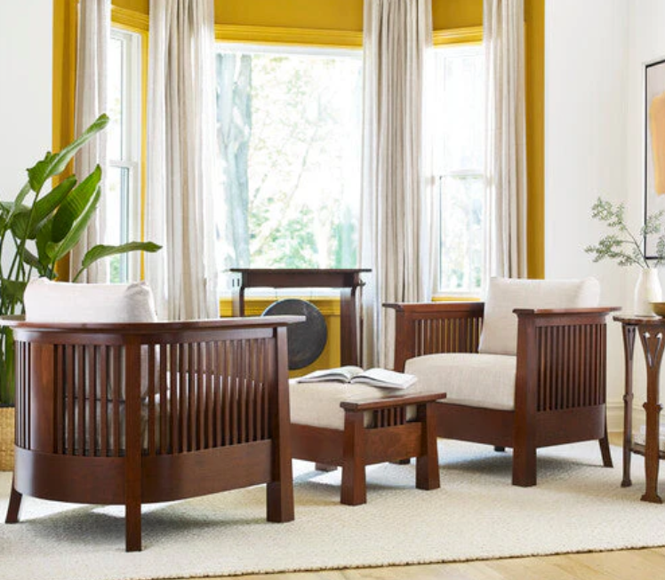 A mid-century modern wooden armchair and matching ottoman in a bright, sunlit room with yellow walls, cream curtains, and a large green plant.