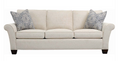A three-seater upholstered loveseat in a light beige fabric, featuring two decorative throw pillows with a gray and white paisley pattern, set against a plain white background.