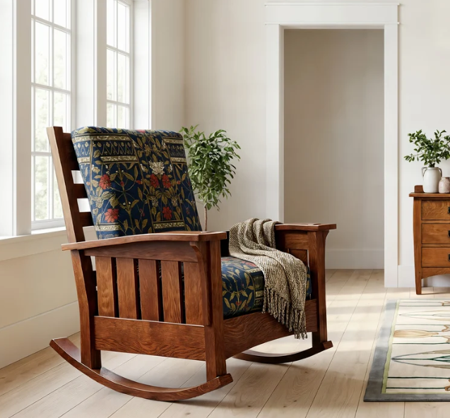 A wooden rocking chair with a dark blue and red floral patterned cushion and a beige throw blanket, set in a bright, modern room with light wood floors and white walls.