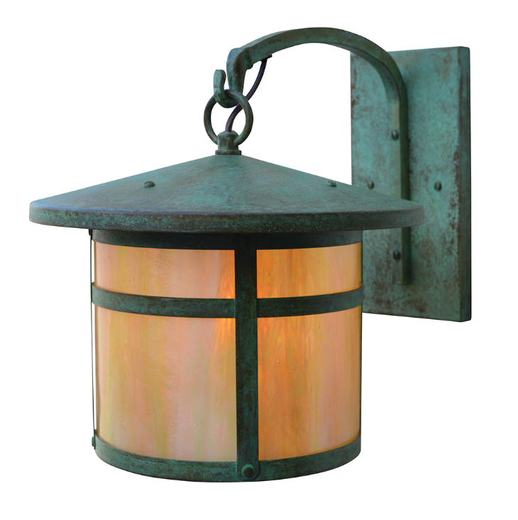 A single outdoor wall sconce with a dark green patina metal frame and a warm orange glowing glass shade, mounted on a matching square wall plate.