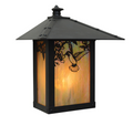 A black metal outdoor lantern light with a pointed roof and warm amber-tinted glass panels featuring a cutout hummingbird and floral design, shown on a plain white background.