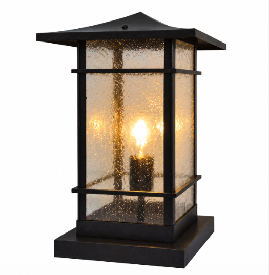 A black outdoor lantern-style light fixture with textured clear glass panels and a warm glowing bulb, shown on a plain white background.