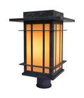 A modern outdoor post cap light fixture with a dark textured metal frame and warm yellow-orange illuminated glass panels, shown on a solid white background.