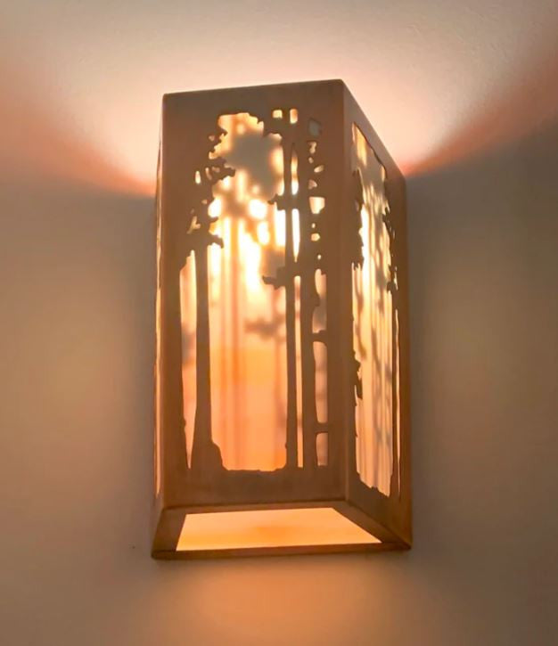 Decorative wall sconce with cut-out design casting a warm glow on a wall.
