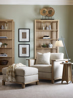 Living room with beige armchair, ottoman, and bookshelves against a light green wall.