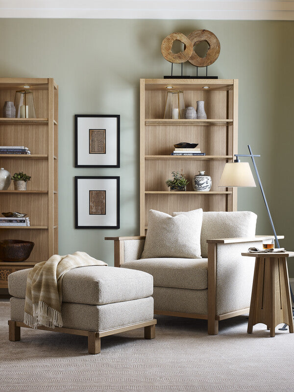 Living room with beige armchair, ottoman, and bookshelves against a light green wall.