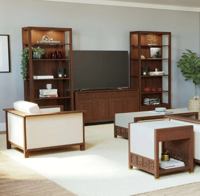 A staged living room featuring a mid-century modern furniture set, including a dark brown wood TV stand, matching shelving units, a low coffee table, and a white armchair with a dark wood frame, all arranged on a light beige rug against a gray wall.