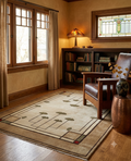 A rectangular area rug with a geometric ginkgo leaf pattern in beige, brown, and gray, styled in a warm, rustic room with a leather armchair, wooden bookcase, and wood floors.