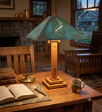 A rustic wooden table lamp with a distressed teal-green metal shade and a warm wood base, styled on a wooden desk in a cozy room with an open book, brass candle holder, and mug.