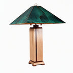 A table lamp with a square wooden pedestal base and a wide, tiered metal shade featuring a distressed green and teal finish with bronze-toned edges, shown against a plain white background.