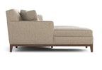 A modern chaise lounge sofa in a textured beige fabric with dark brown wooden legs, shown from a side profile view on a white background.