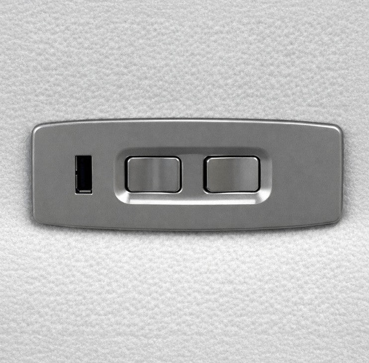 A rectangular brushed metal control panel with two toggle switches and a small vertical slot, mounted on a textured white surface.