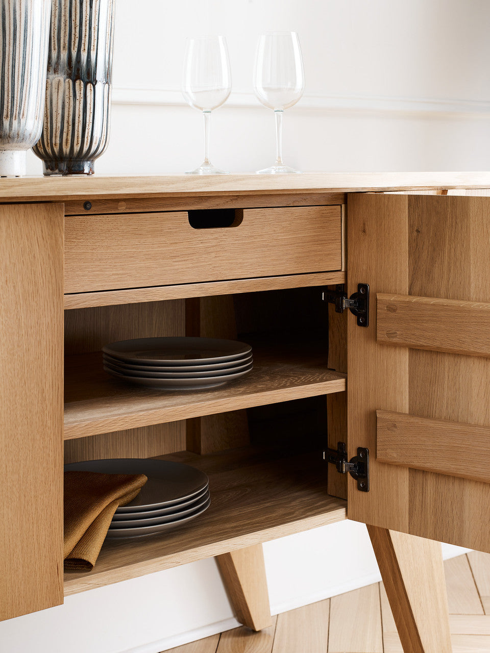 Wooden kitchen cabinet with open door revealing shelves and plates inside.