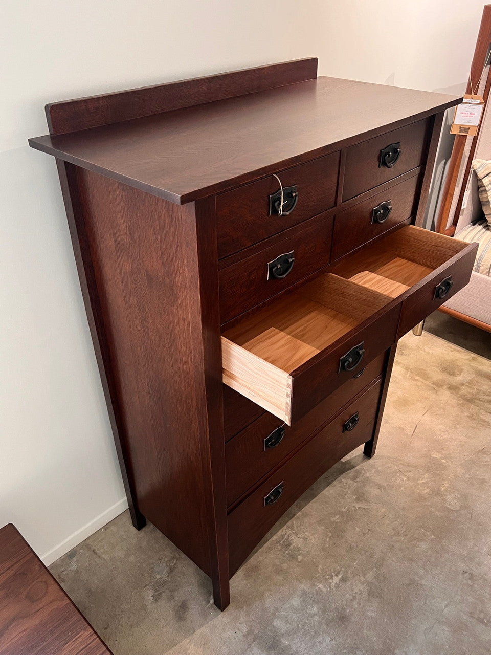 Wooden dresser with open drawer on a concrete floor against a white wall