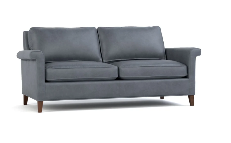 A modern two-seater loveseat sofa upholstered in dark gray fabric, featuring rolled arms, two thick back cushions, two seat cushions, and dark brown wooden legs, shown against a plain white background.